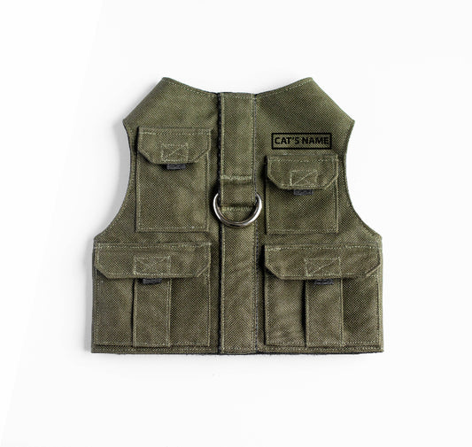 Khaki green pet harness designed with a utility vest appearance, featuring several small pockets, a leash attachment ring, and a customizable name patch.