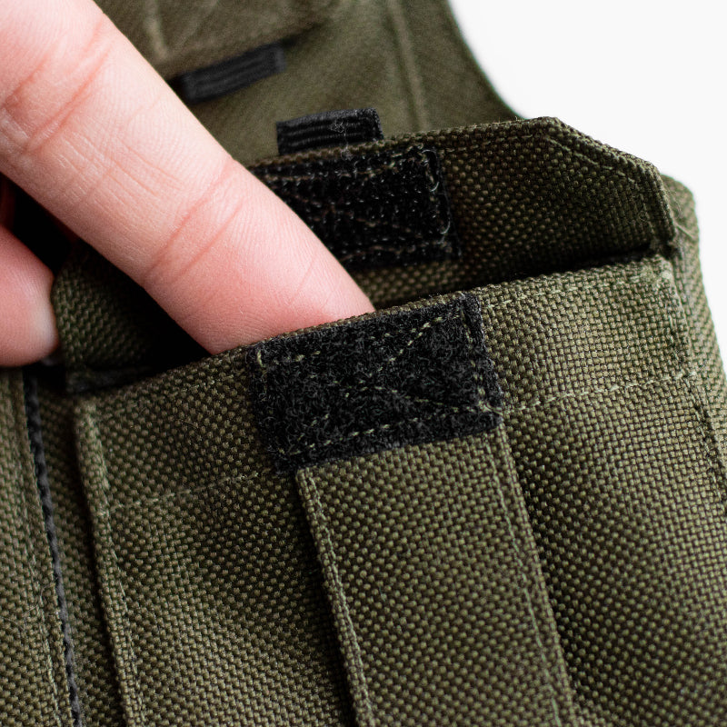 Khaki green pet harness designed with a utility vest appearance, featuring several small pockets, a leash attachment ring, and a customizable name patch.