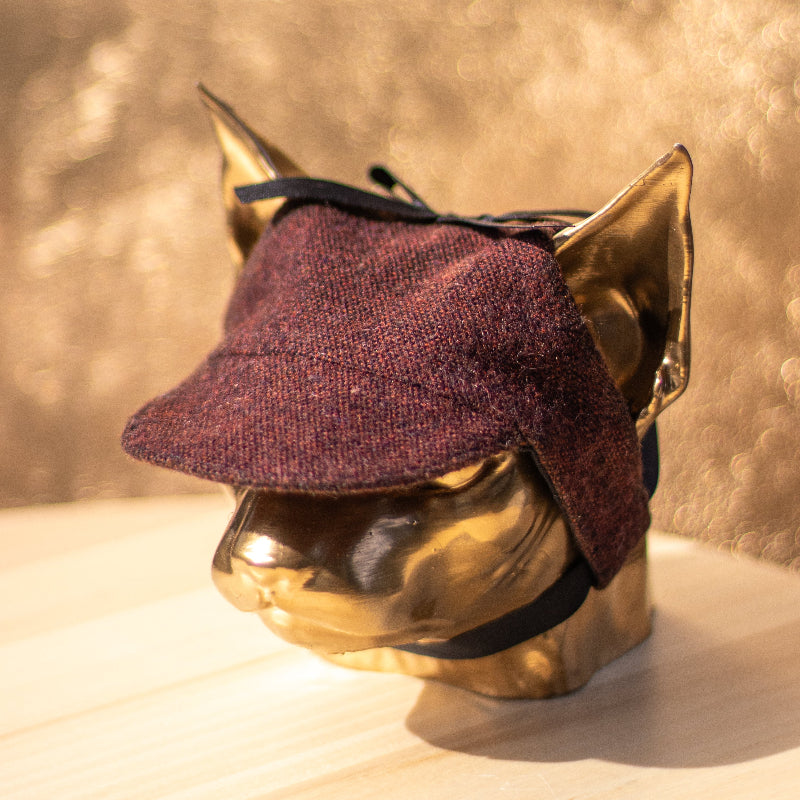 Tweed-style hat for a cat with a small brim and a black ribbon tied in a bow on top, shown on a grey textured surface.