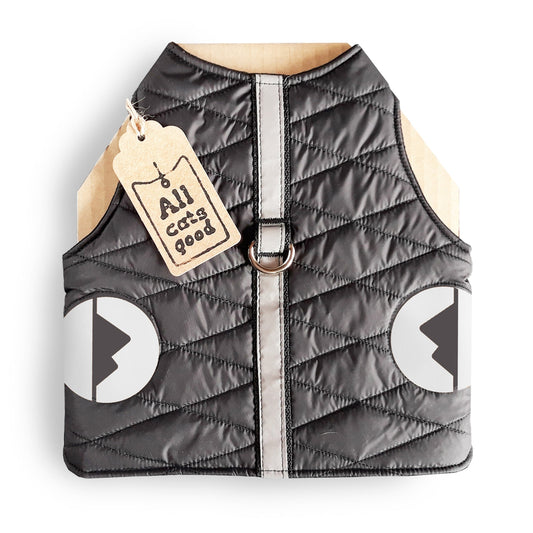 A quilted black cat harness with reflective silver stripes, circular reflective elements, and a brown "Allcatsgood" tag.