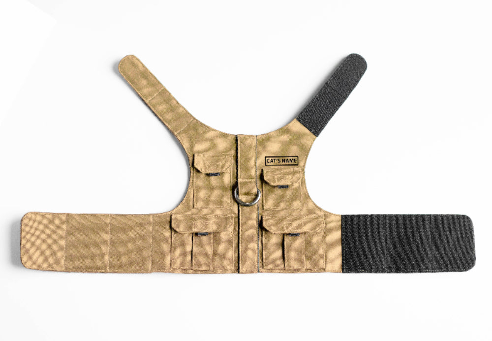 Tan pet harness designed with a utility vest appearance, featuring several small pockets, a leash attachment ring, and a customizable name patch.