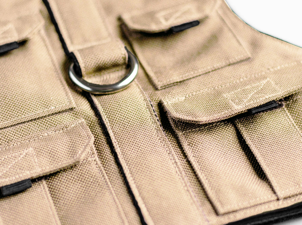 Tan pet harness designed with a utility vest appearance, featuring several small pockets, a leash attachment ring, and a customizable name patch.