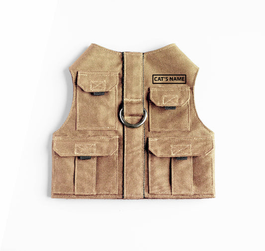 Tan pet harness designed with a utility vest appearance, featuring several small pockets, a leash attachment ring, and a customizable name patch.