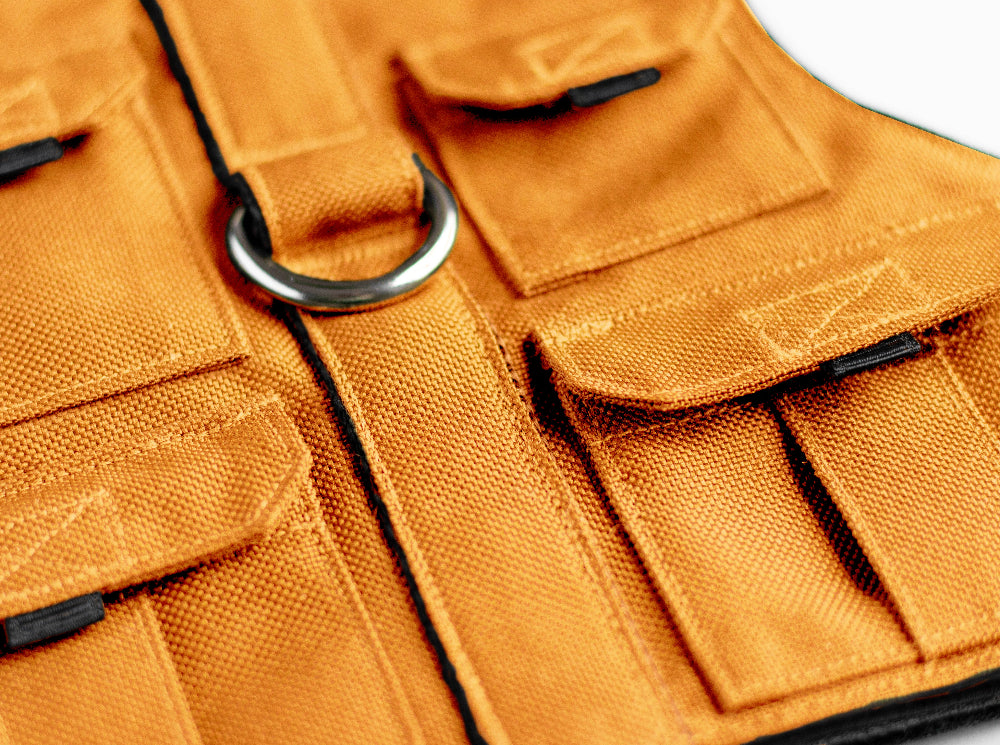 Cat harness designed with a utility vest appearance, featuring several small pockets, a leash attachment ring, and a customizable name patch.