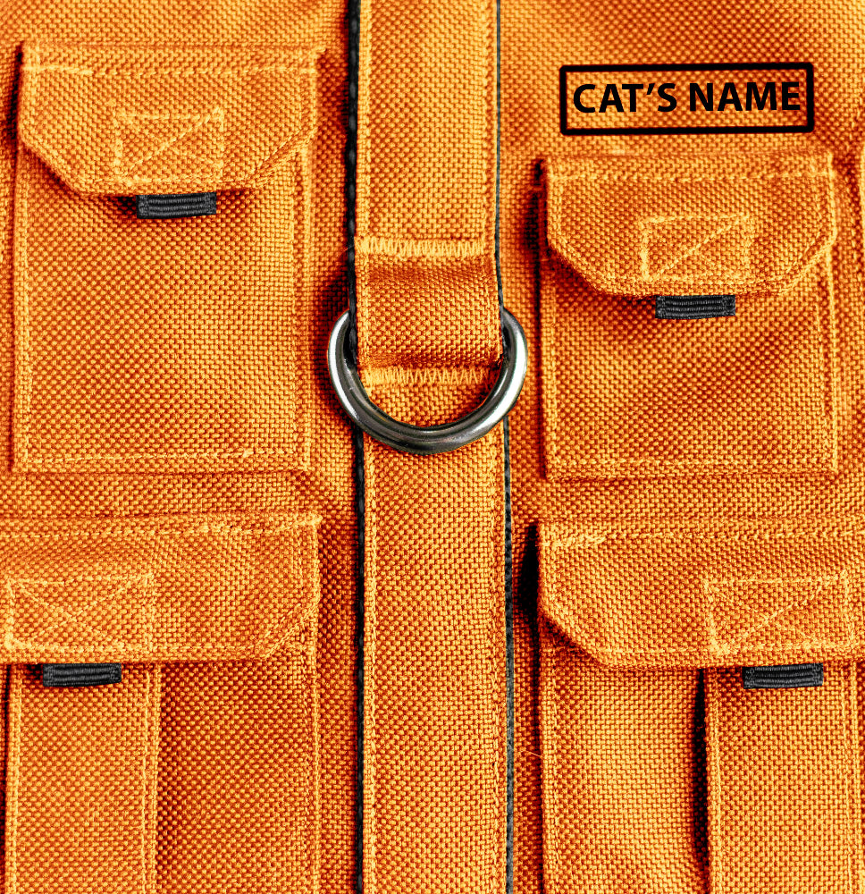 Cat harness designed with a utility vest appearance, featuring several small pockets, a leash attachment ring, and a customizable name patch.