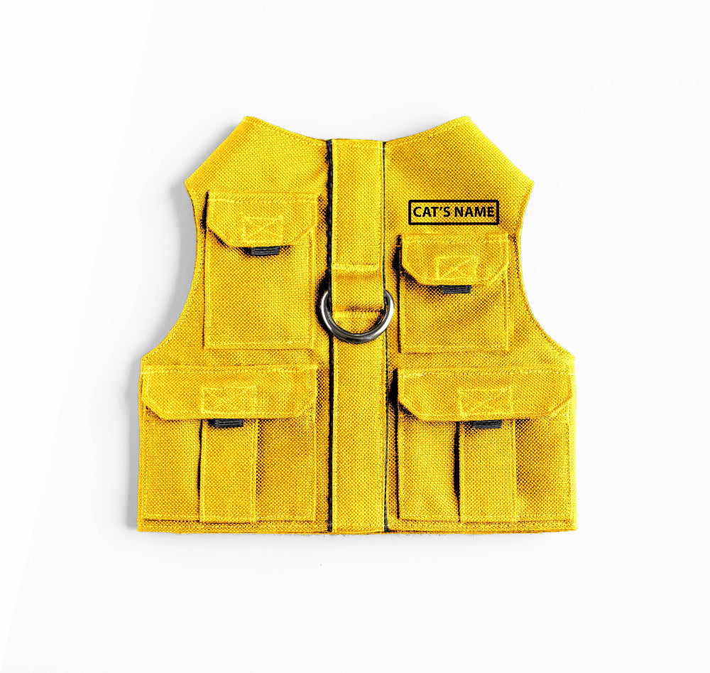 Cat harness designed with a utility vest appearance, featuring several small pockets, a leash attachment ring, and a customizable name patch.