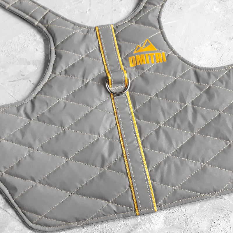 A quilted light grey cat harness with yellow trim, a reflective stripe, personalized yellow "DMITRI" text with a mountain icon