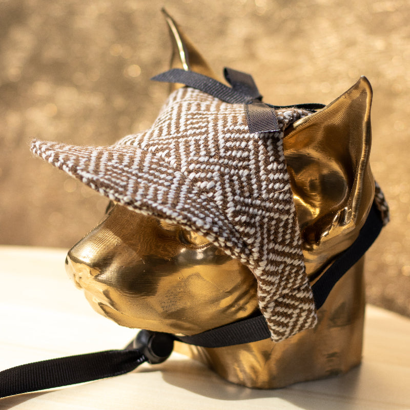 Tweed-style hat for a cat with a small brim and a black ribbon tied in a bow on top, shown on a grey textured surface.