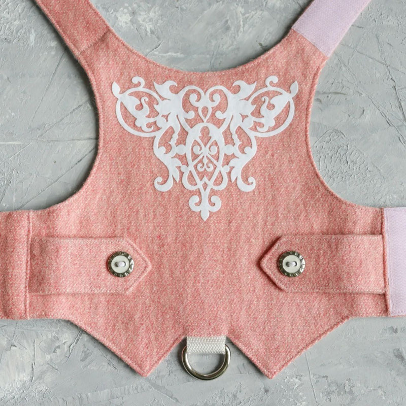 Close-up of a pink tweed cat harness with white decorative embroidery on the back, silver and white buttons, and a silver D-ring.