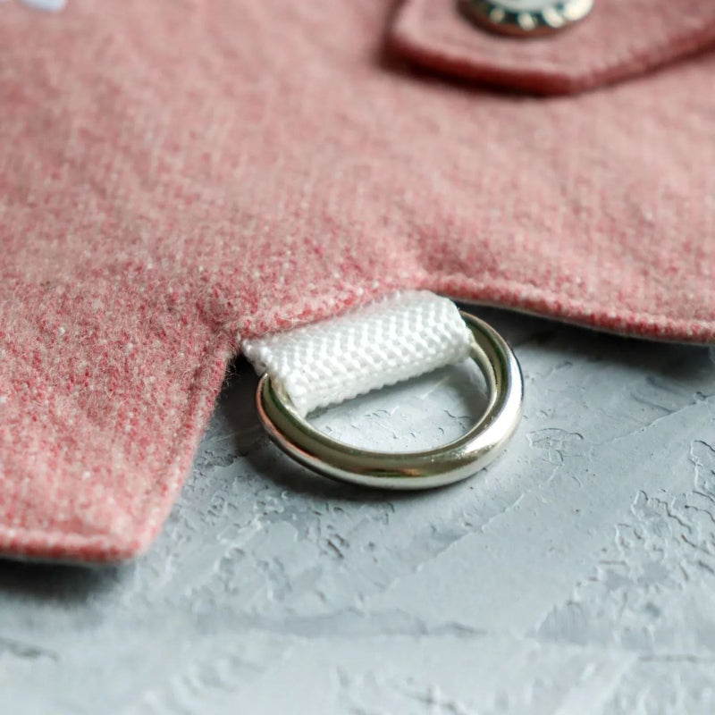 Close-up of a silver metal D-ring attached with white stitching to a pink tweed cat harness.