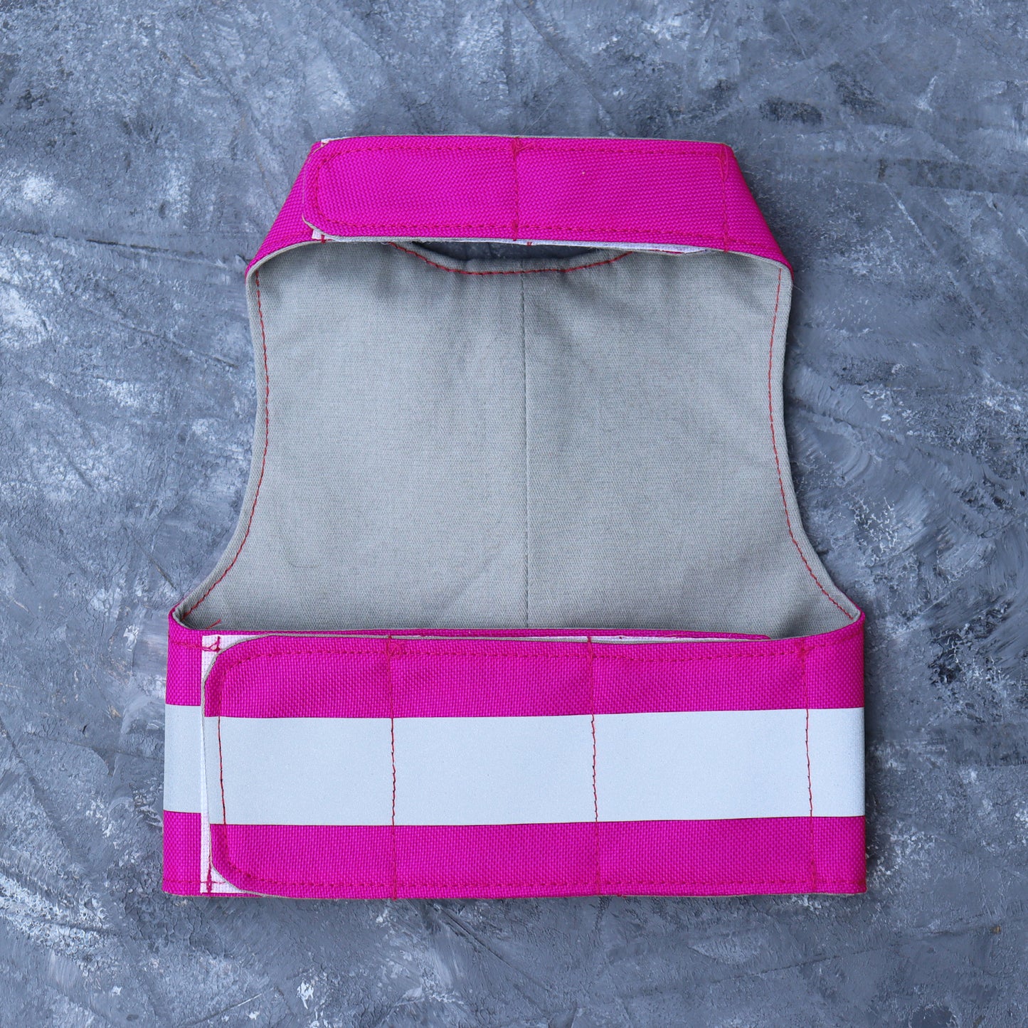 A bright pink cat harness with horizontal reflective silver stripes, a grey vertical strap, and a silver D-ring