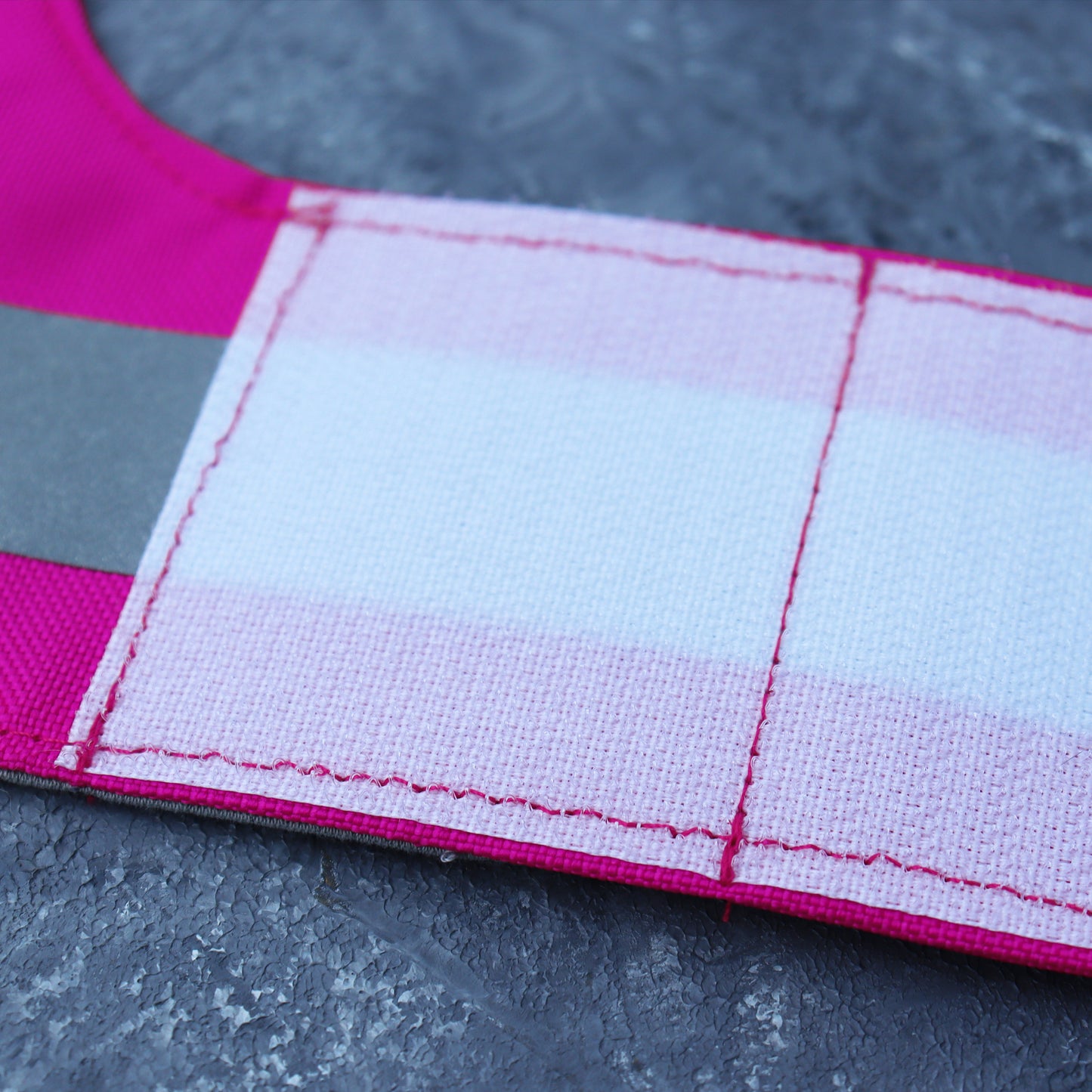 A bright pink cat harness with horizontal reflective silver stripes, a grey vertical strap, and a silver D-ring