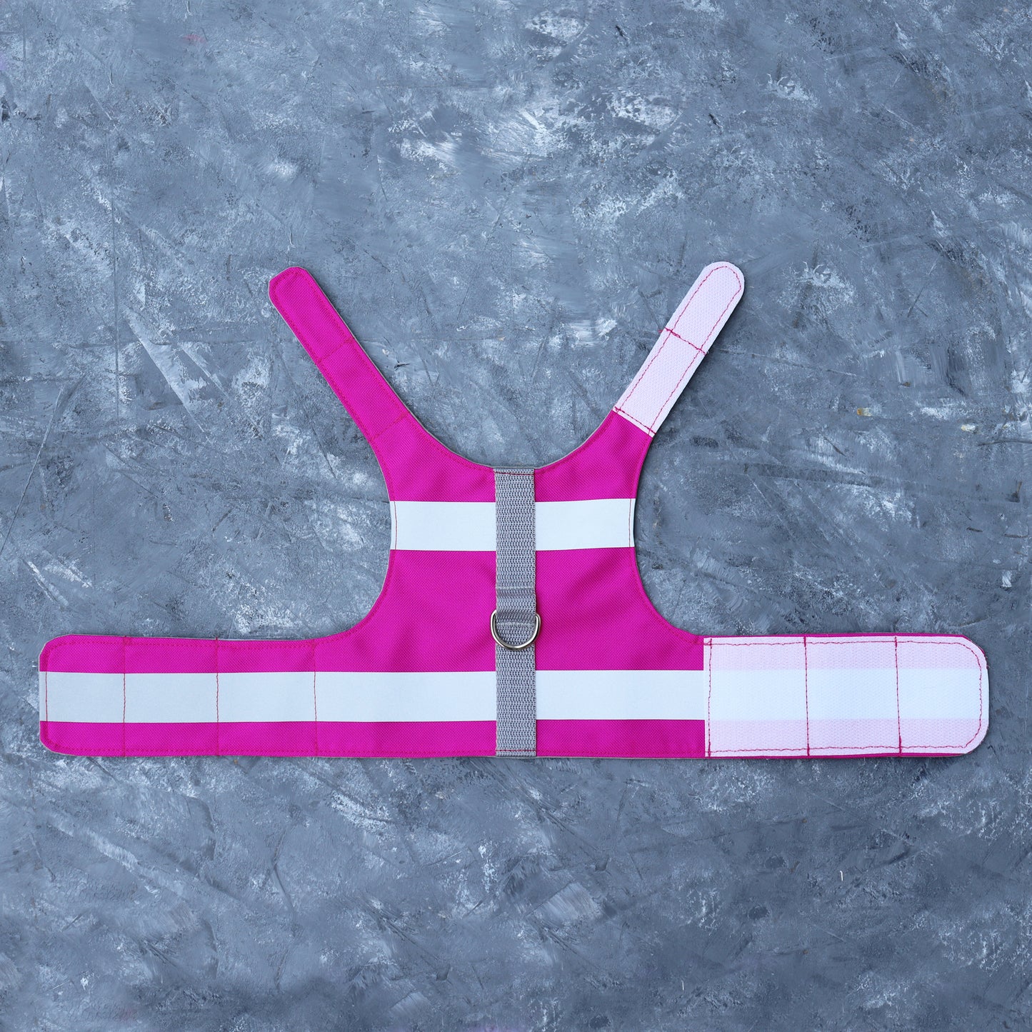 A bright pink cat harness with horizontal reflective silver stripes, a grey vertical strap, and a silver D-ring