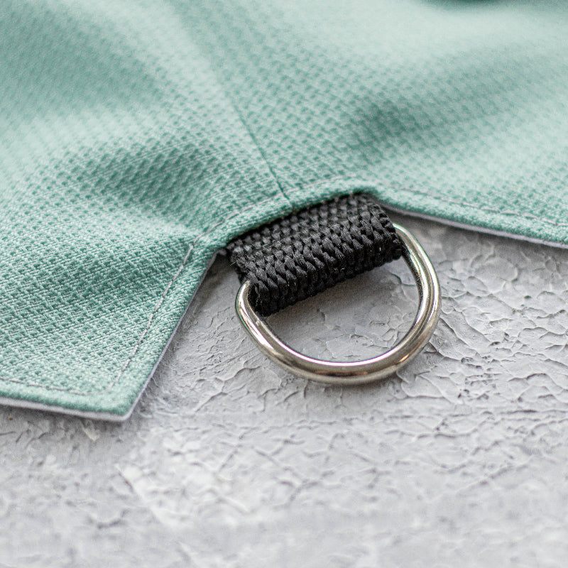 Close-up of a silver metal D-ring attached to a black nylon loop on an azure textured cat harness.