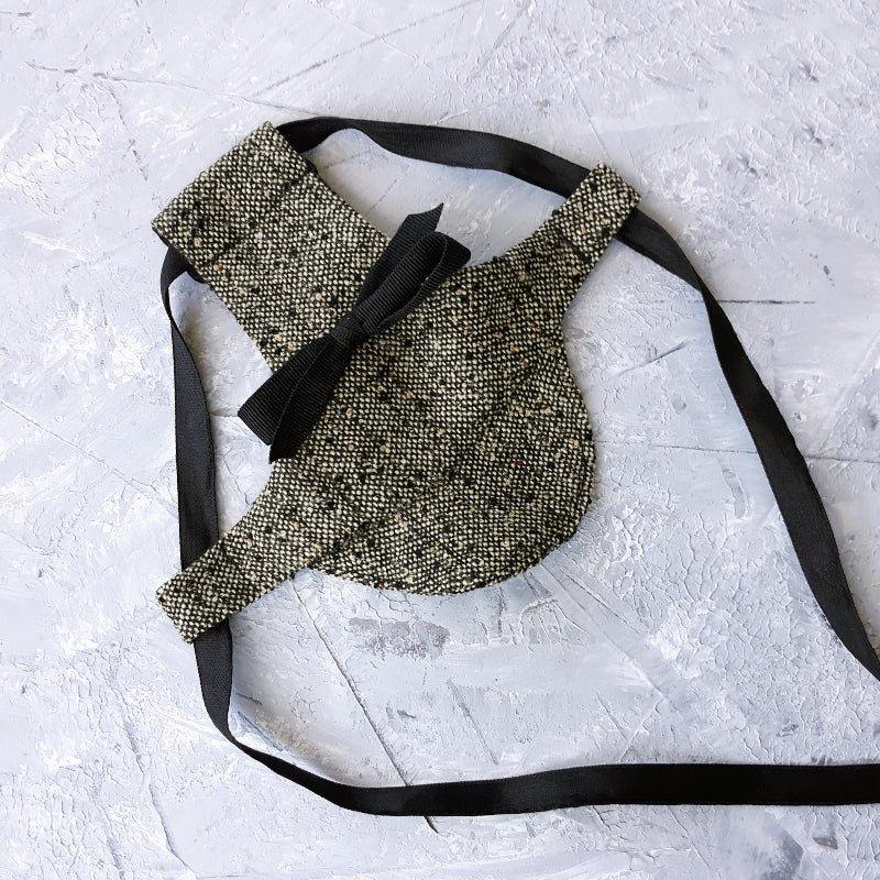 Tweed-style hat for a cat with a small brim and a black ribbon tied in a bow on top, shown on a grey textured surface.