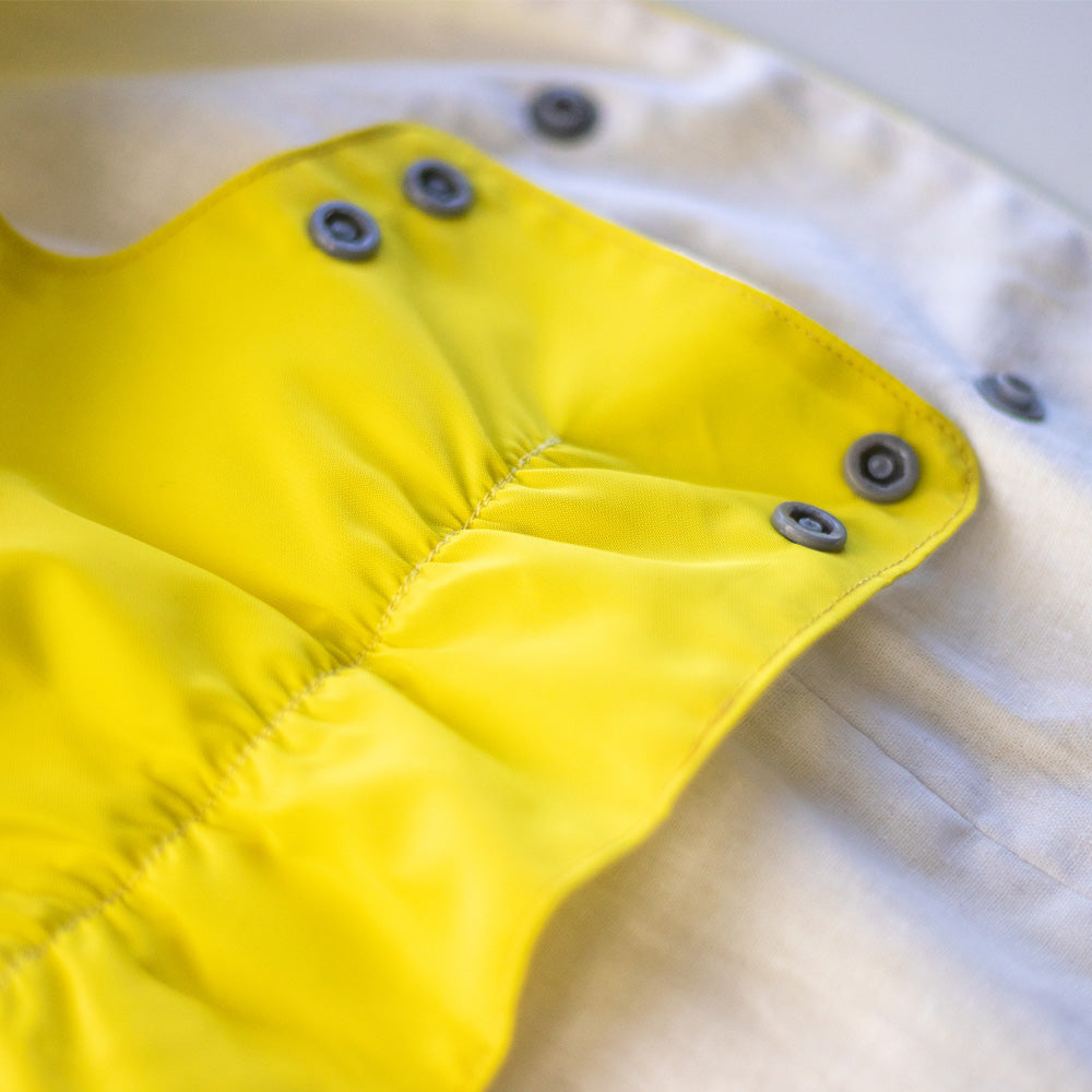 Close-up of grey snap closures on a bright yellow cat raincoat, showing the fabric and stitching details.