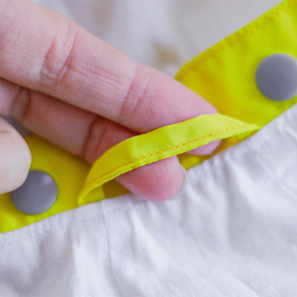 Close-up of grey snap closures on a bright yellow cat raincoat, showing the fabric and stitching details.