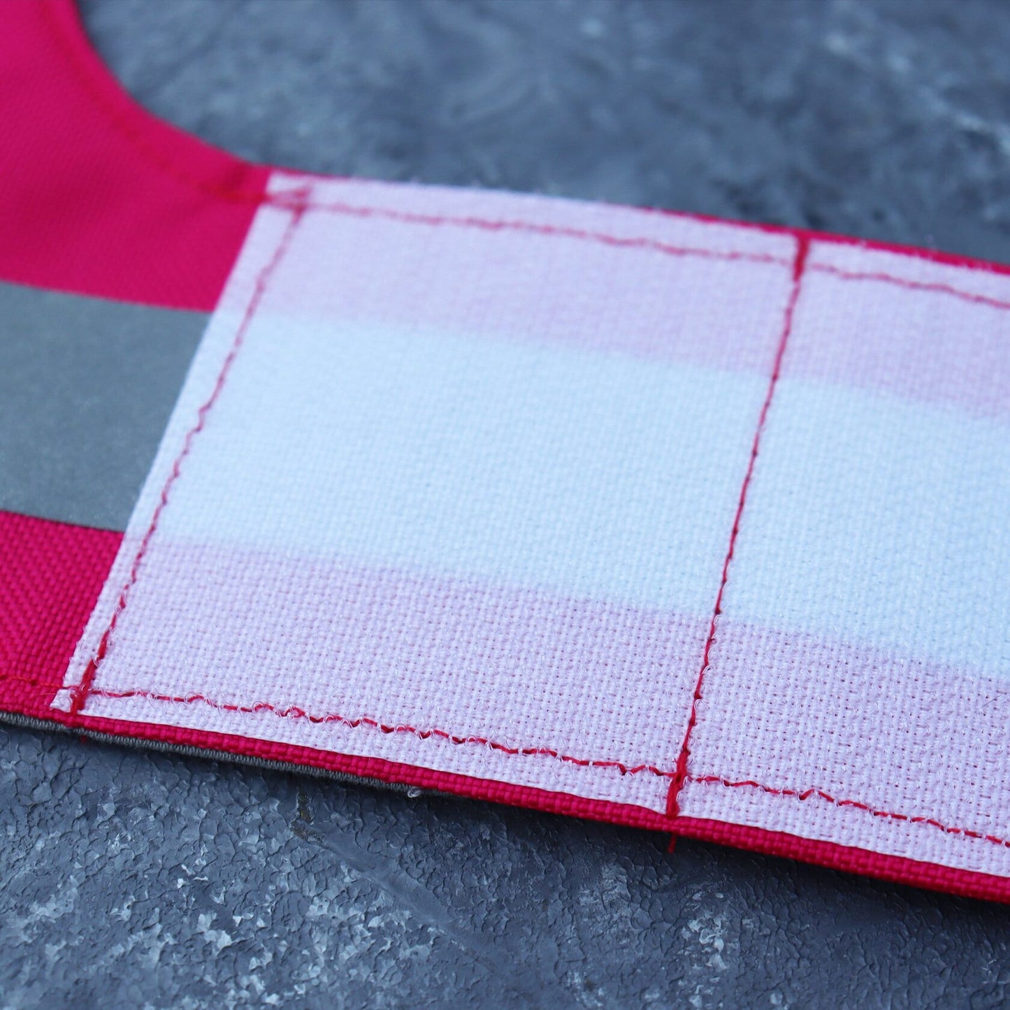 A close-up view of the white Velcro closure on a bright pink high-visibility cat harness strap, illustrating how the harness can be adjusted and secured for safety.
