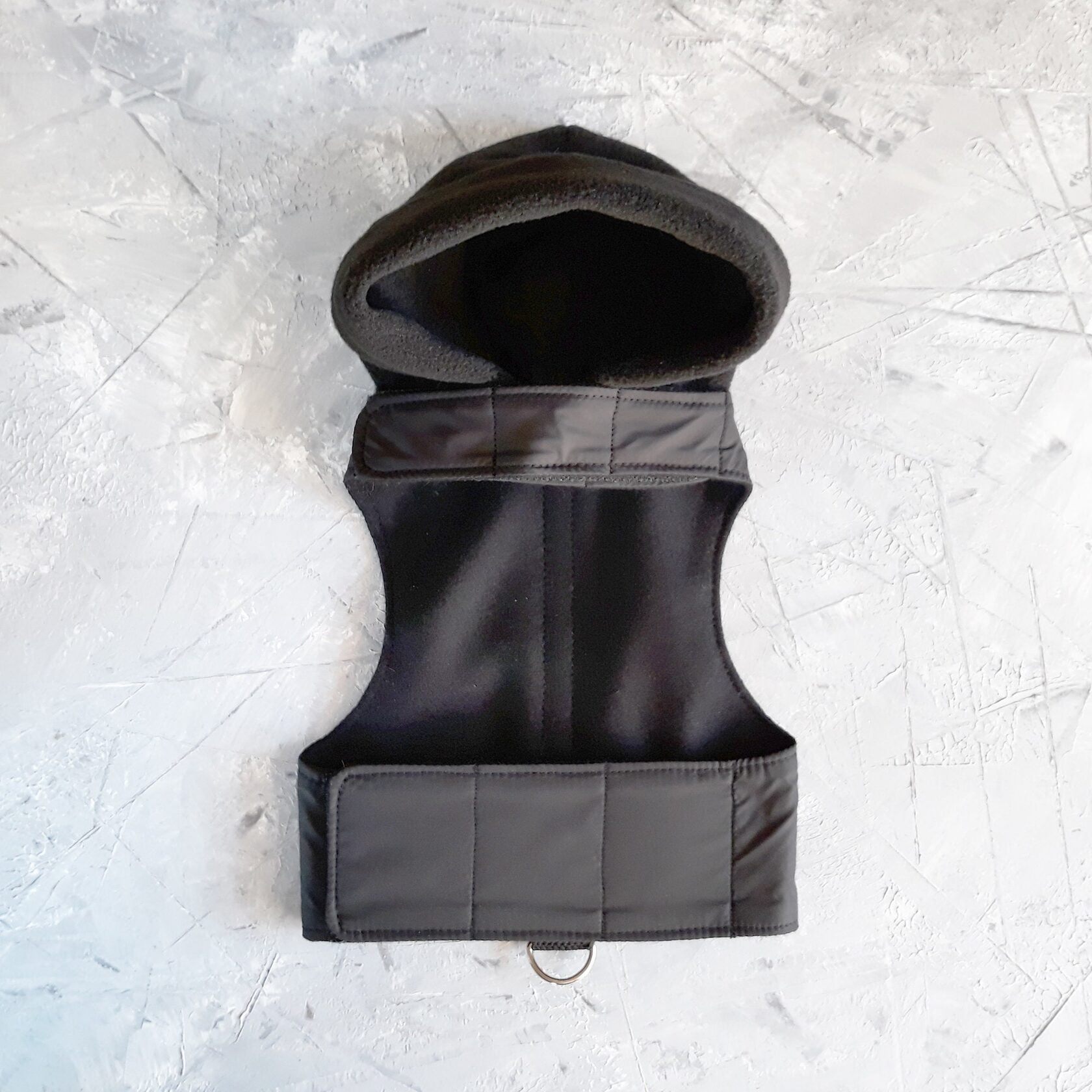 A black cat harness with a soft, fleece-lined hood and a D-ring for leash attachment.