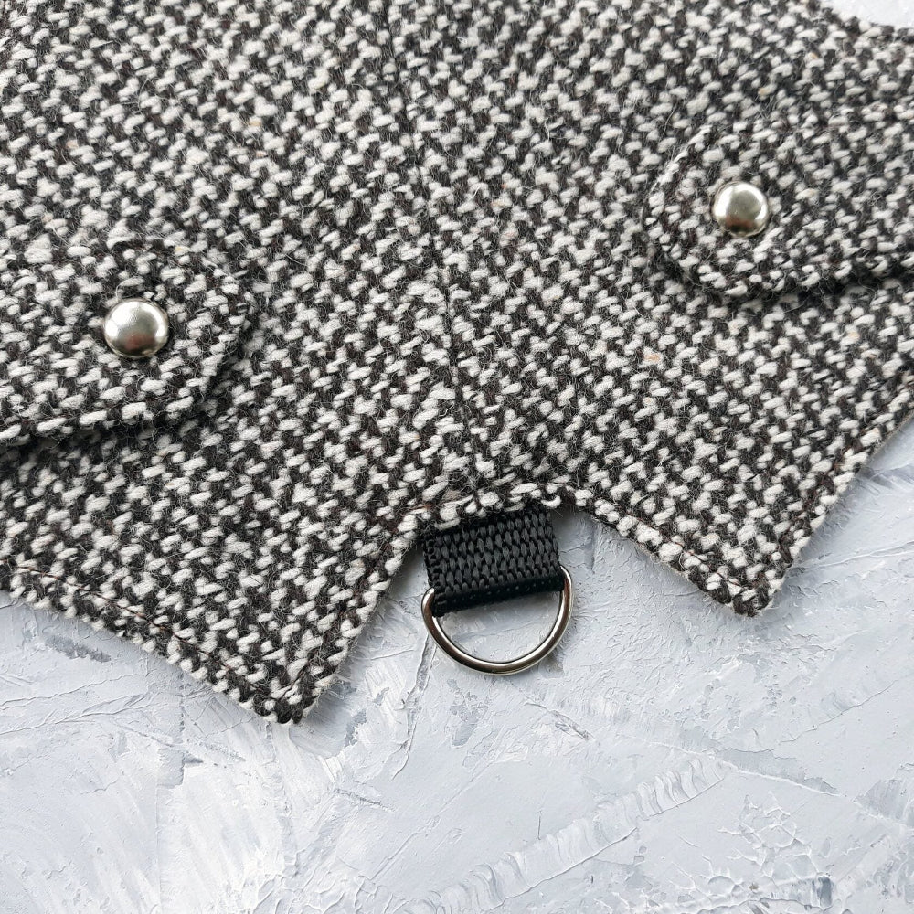 Close-up of a black metal D-ring and silver decorative buttons on a black and white houndstooth cat harness.