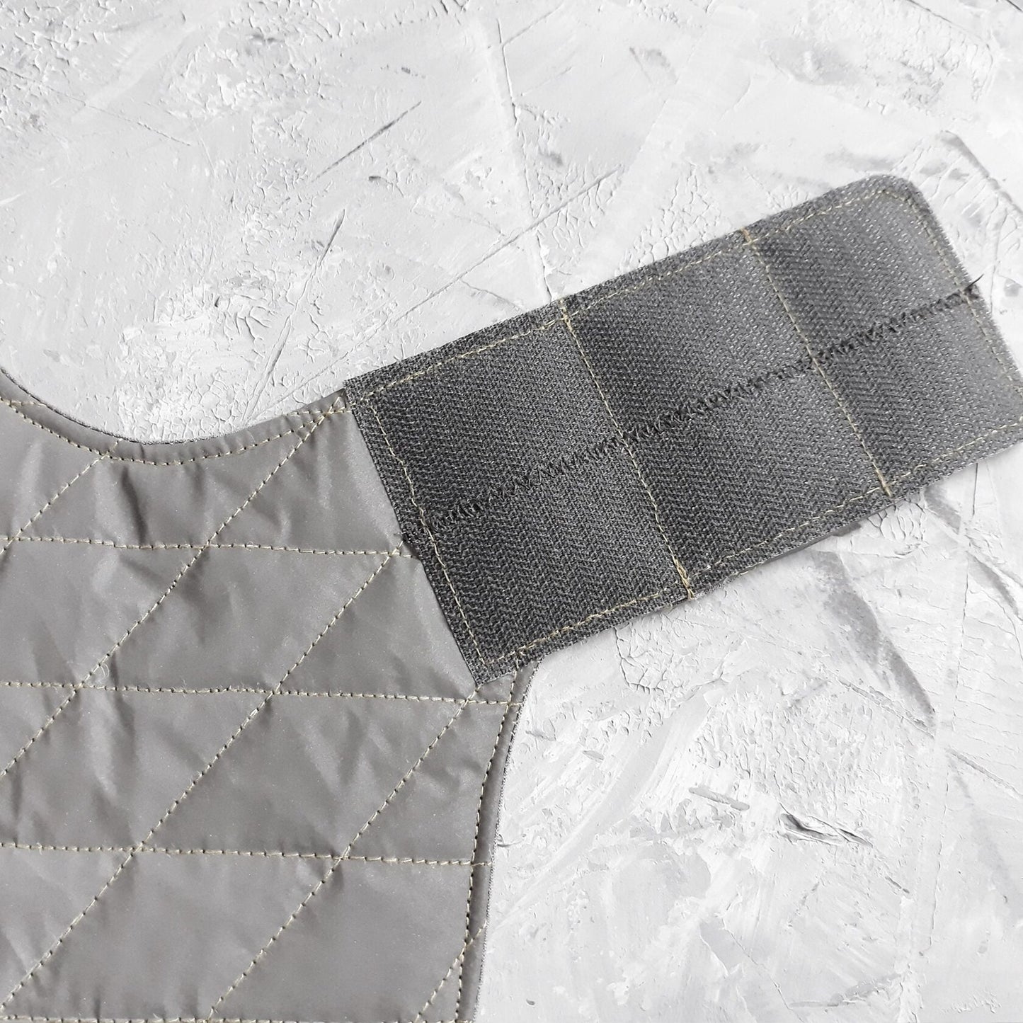 Close-up of a grey Velcro strap attached to a light grey quilted cat harness.