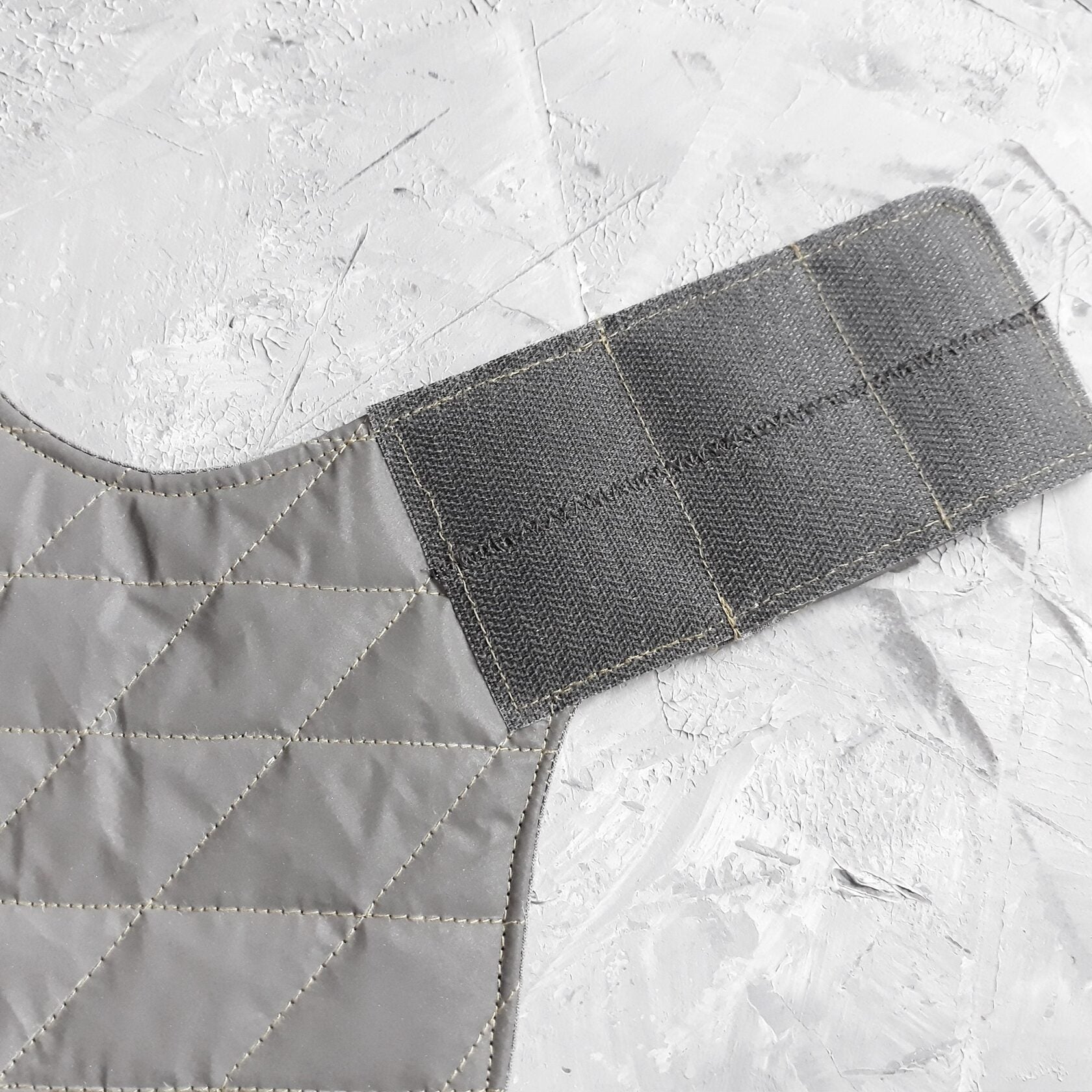 Close-up of a grey Velcro strap attached to a light grey quilted cat harness.