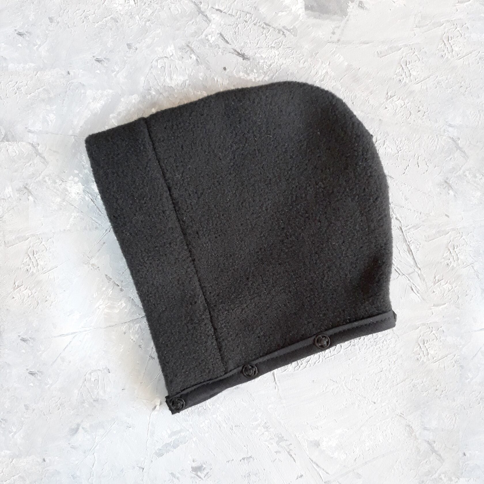 A black cat harness with a soft, fleece-lined hood and a D-ring for leash attachment.