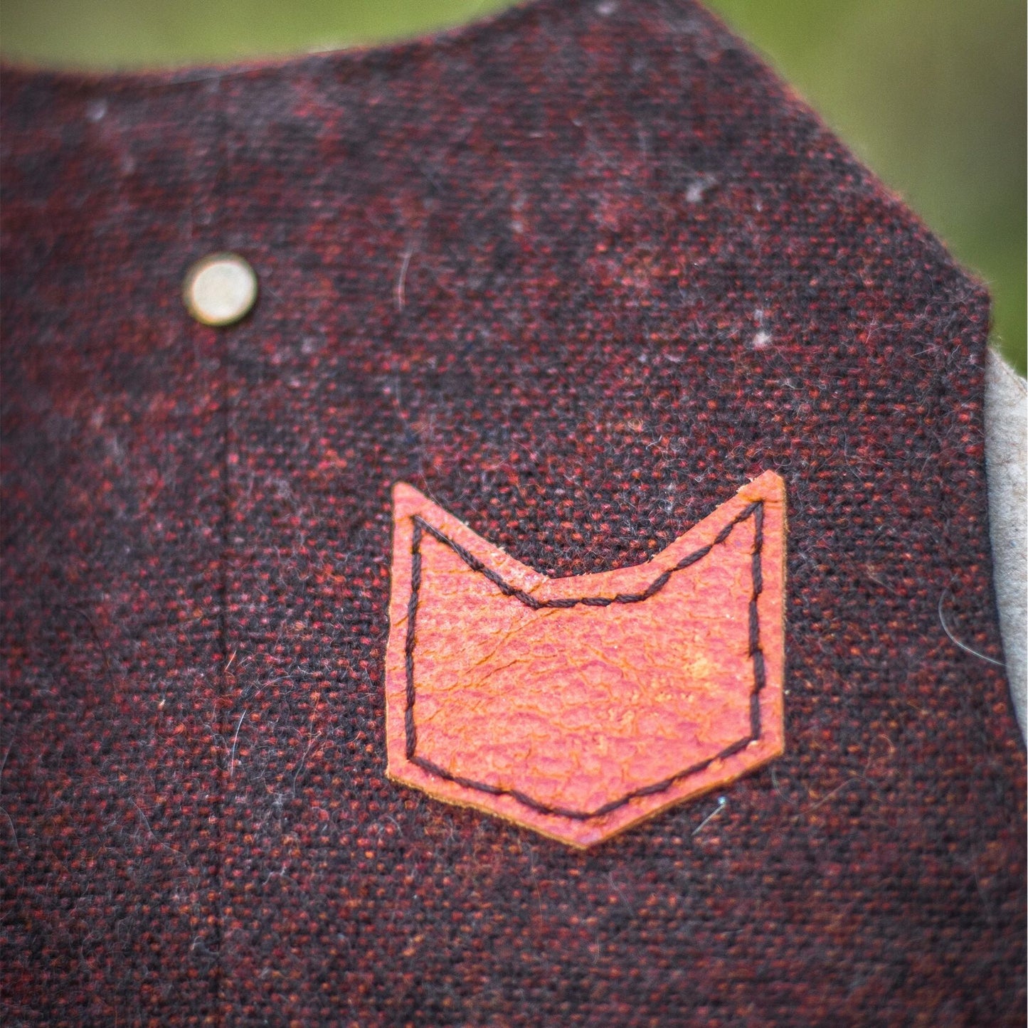 Close-up of a brown faux leather patch in the shape of a cat's head on a burgundy tweed cat harness.