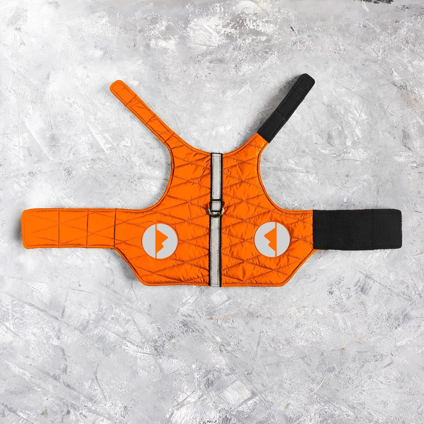 A flat lay of a quilted orange cat harness with a central vertical reflective silver stripe, round reflective patches with arrow designs, and black Velcro closures.