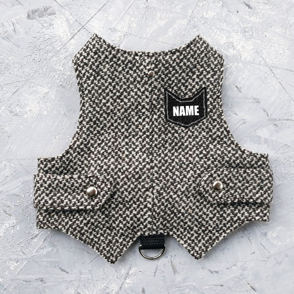 A black and white houndstooth cat harness with silver decorative buttons, a black D-ring, and a customizable black patch labeled "NAME".