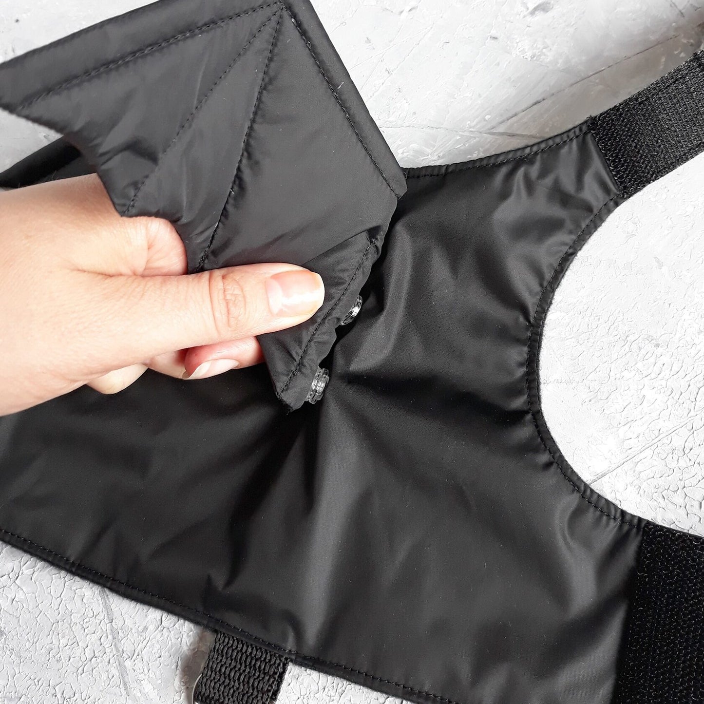 Detailed view of a black cat harness where a hand interacts with one of the attached bat wings, showcasing the material and design of the wing.