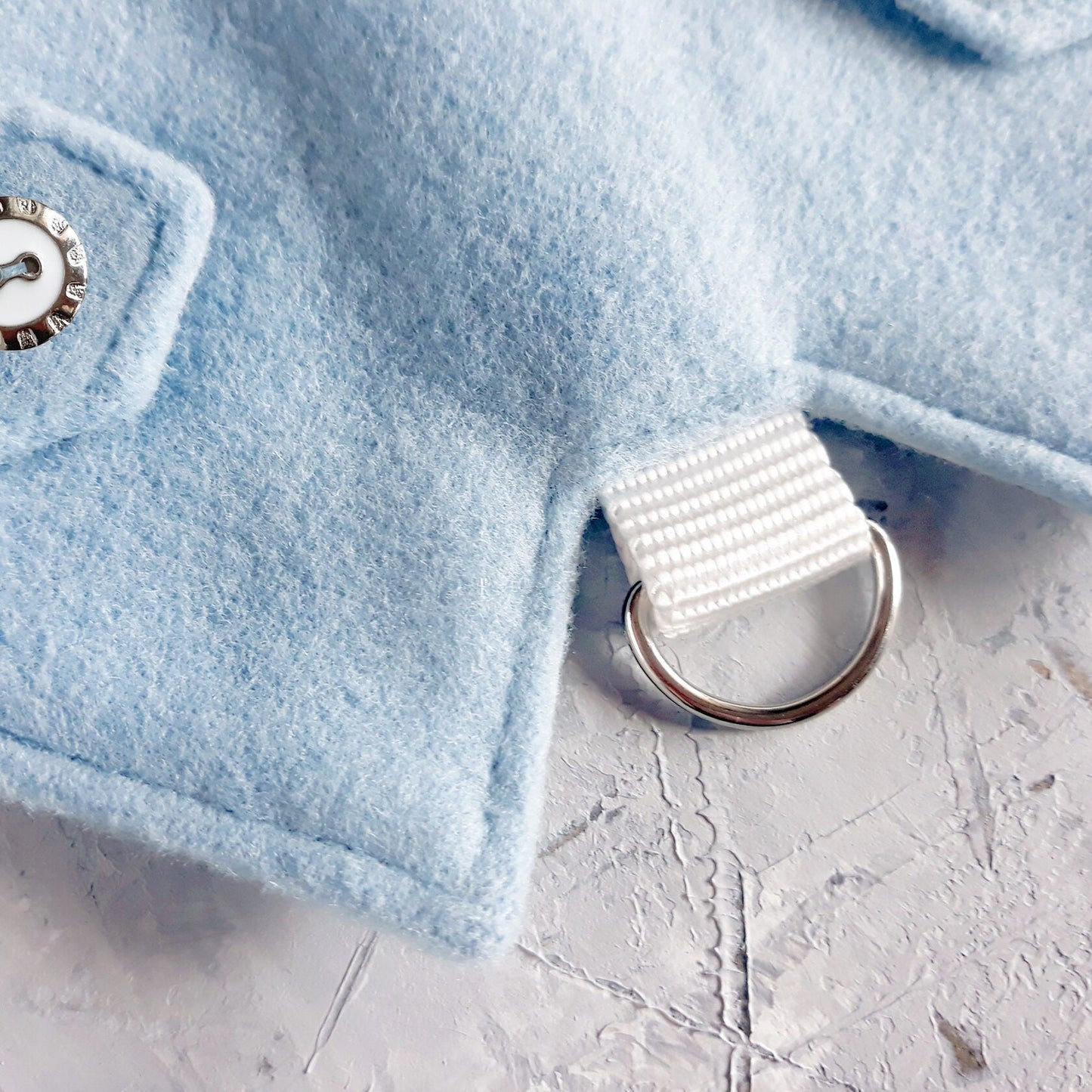 Silver D-ring for leash attachment on a light blue cat harness, connected by a white fabric loop.