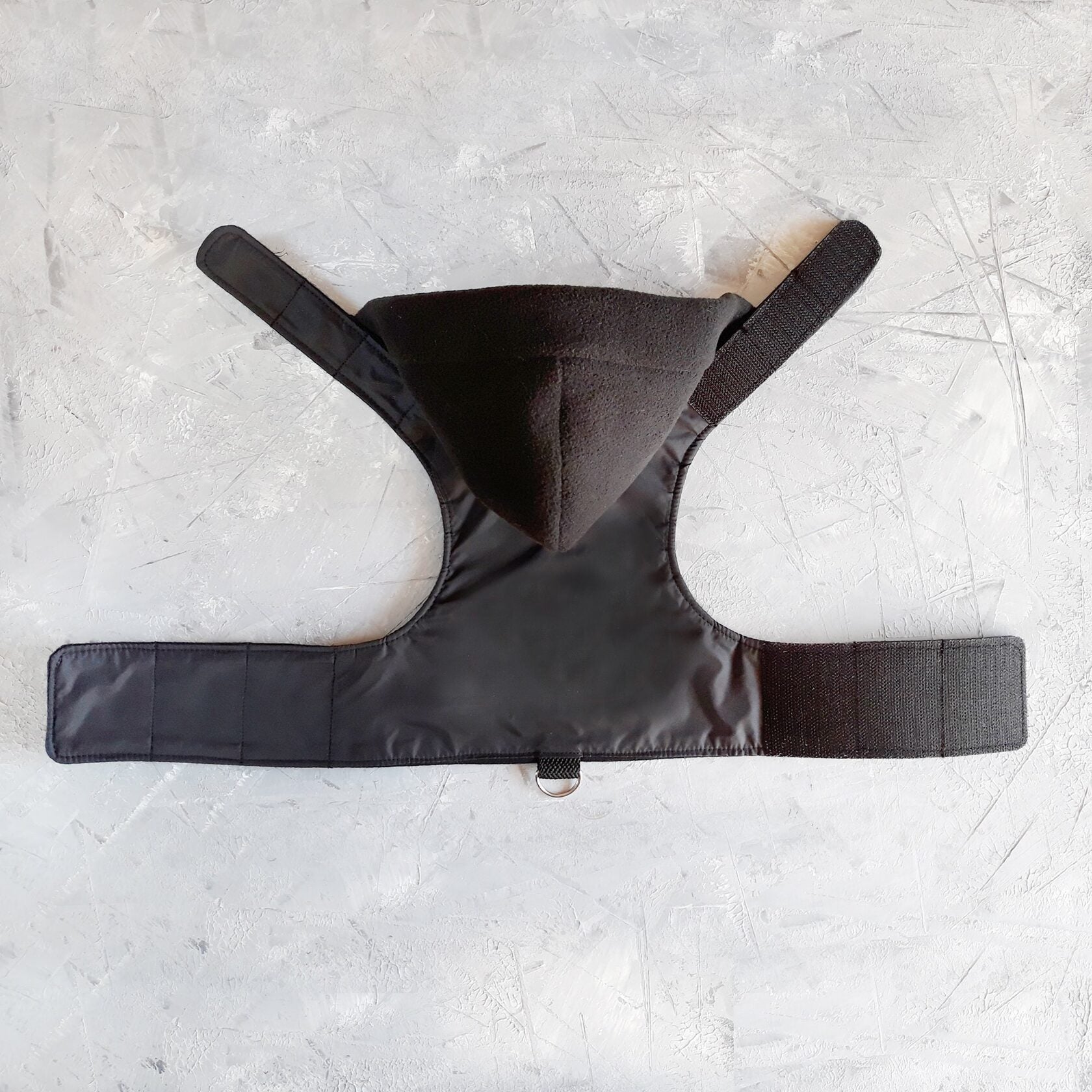 A black cat harness with a soft, fleece-lined hood and a D-ring for leash attachment.