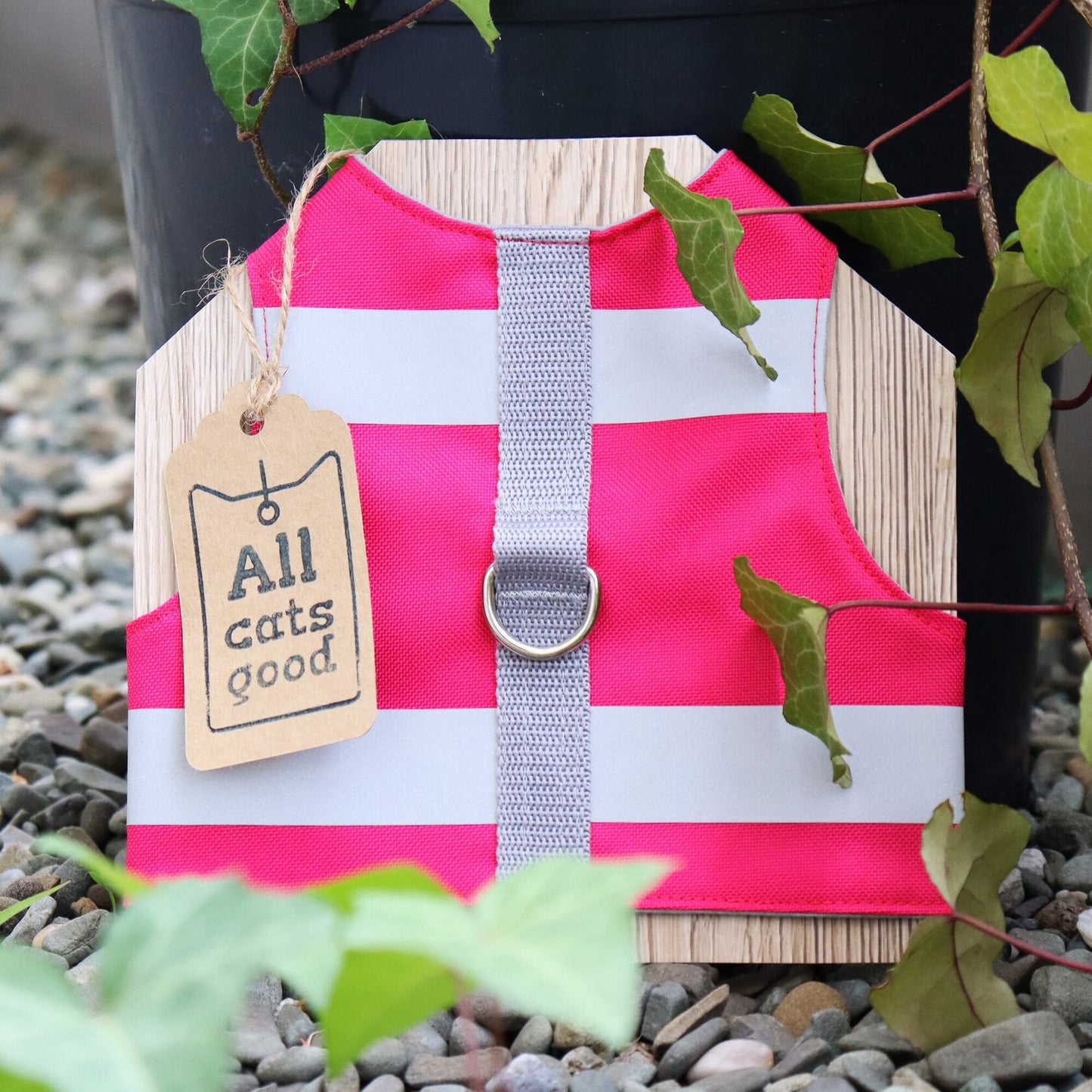 A bright pink, high-visibility, potentially water-repellent cat safety harness with two horizontal silver reflective stripes. It features a grey central strap and a metal D-ring for leash attachment. This harness is designed for safety and visibility.