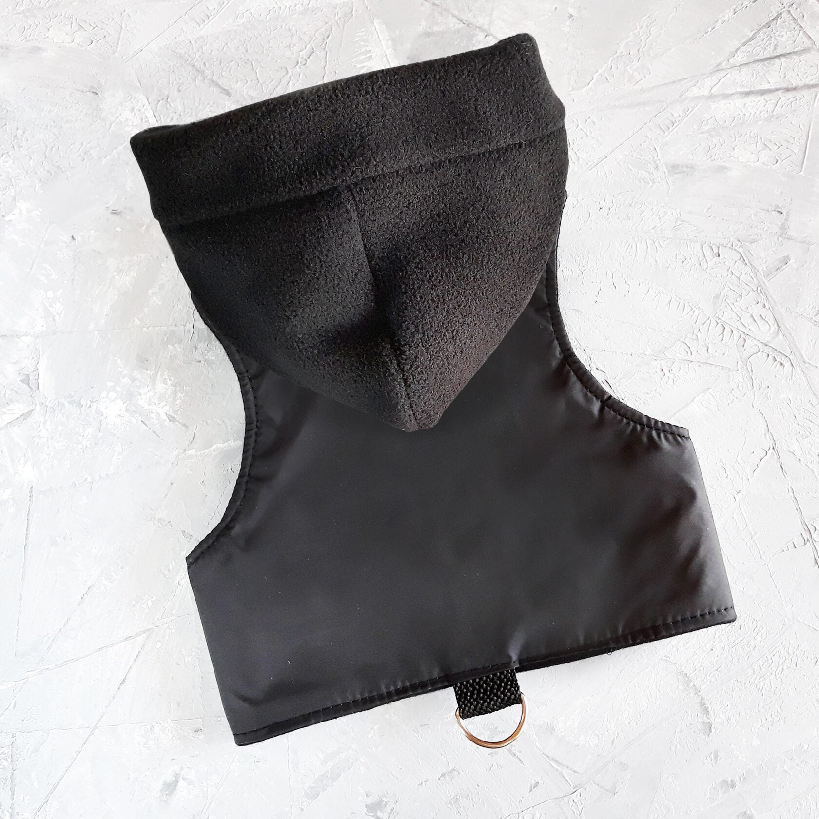 A black cat harness with a soft, fleece-lined hood and a D-ring for leash attachment.