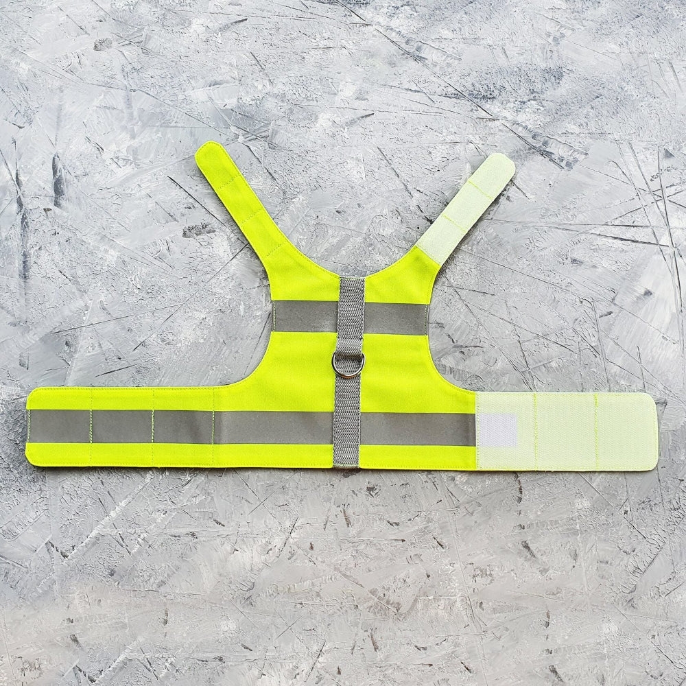 Flat lay of a neon yellow Escape proof cat safety harness with horizontal silver reflective stripes and a grey vertical strap with a D-ring.