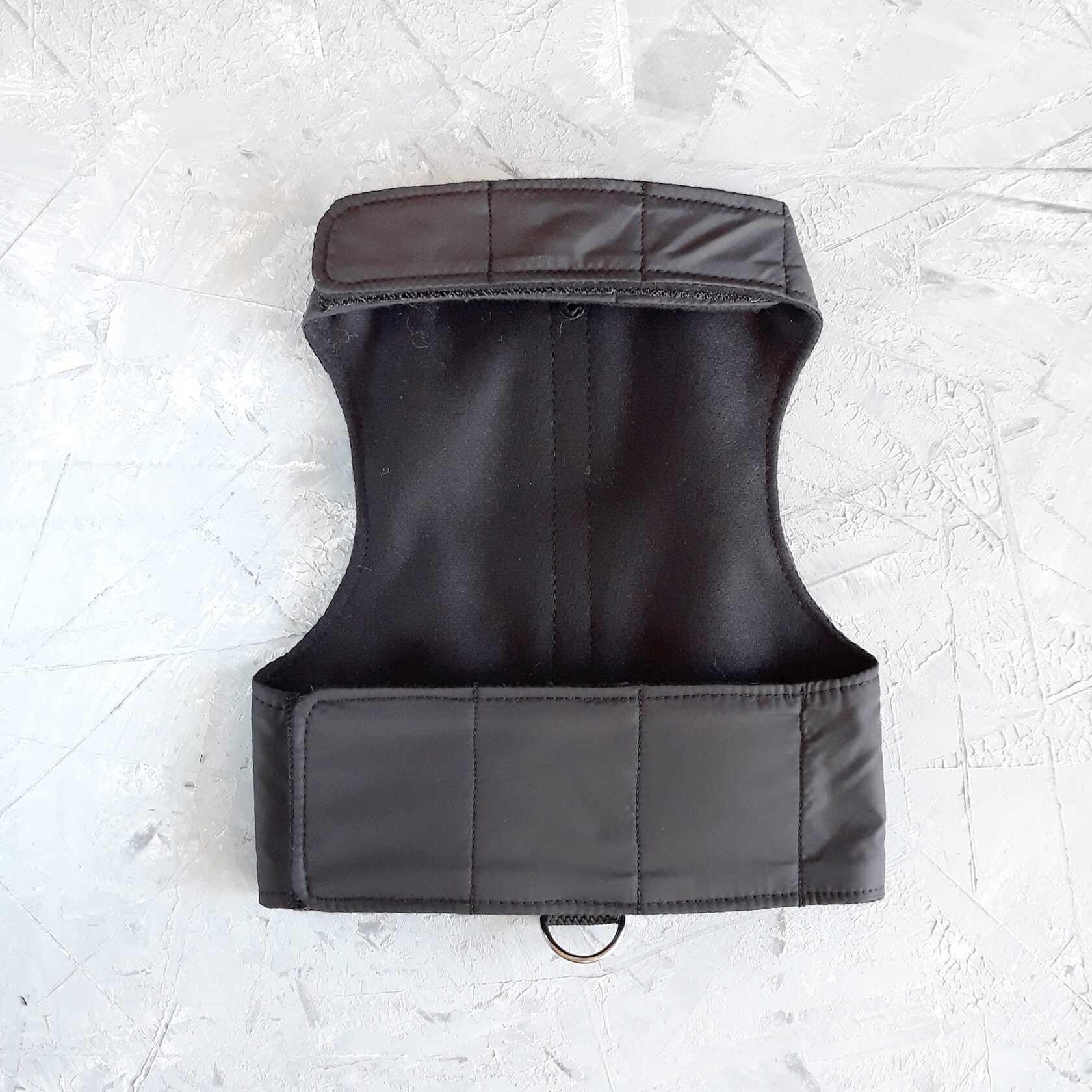 A black cat harness with a soft, fleece-lined hood and a D-ring for leash attachment.