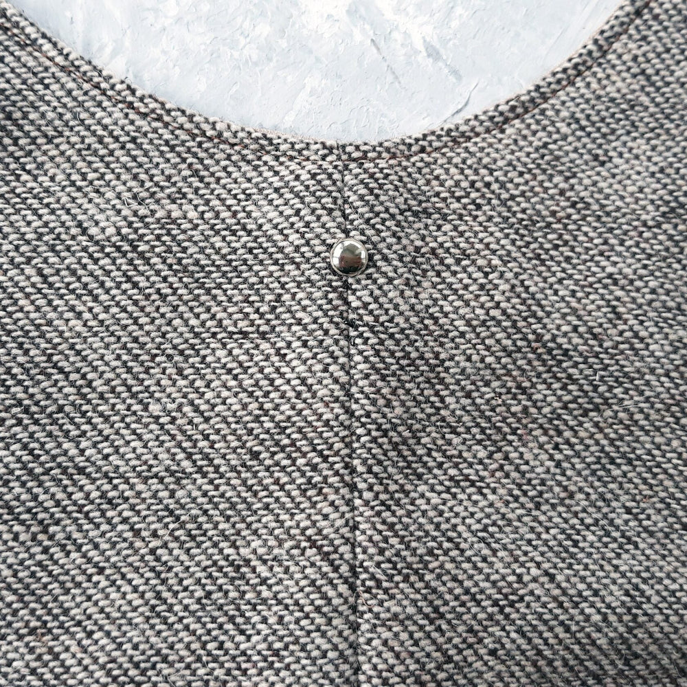 Close-up of a silver snap closure on a light brown tweed cat harness.