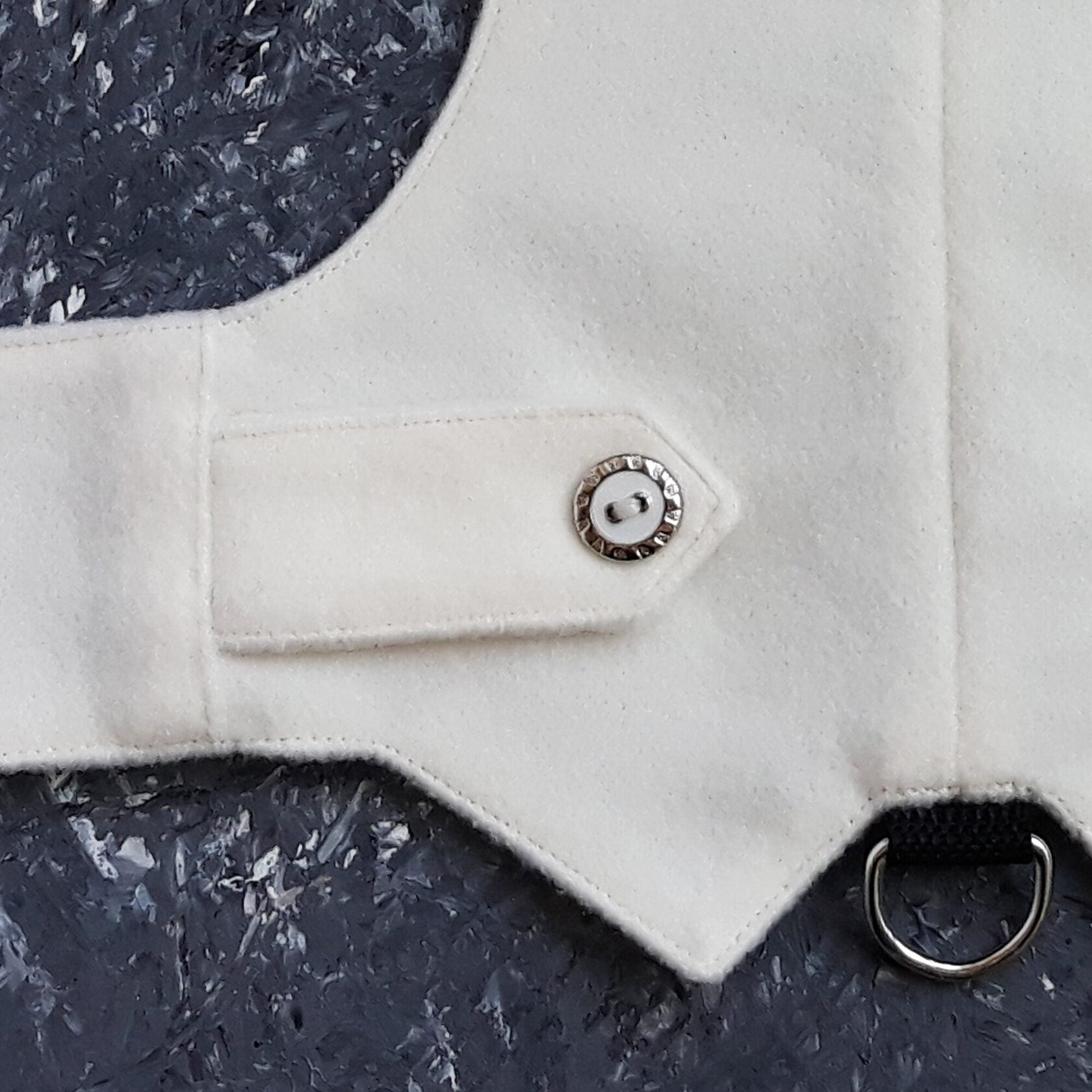 A close-up view showing the snap button fastening and the leash attachment D-ring on a white cat harness