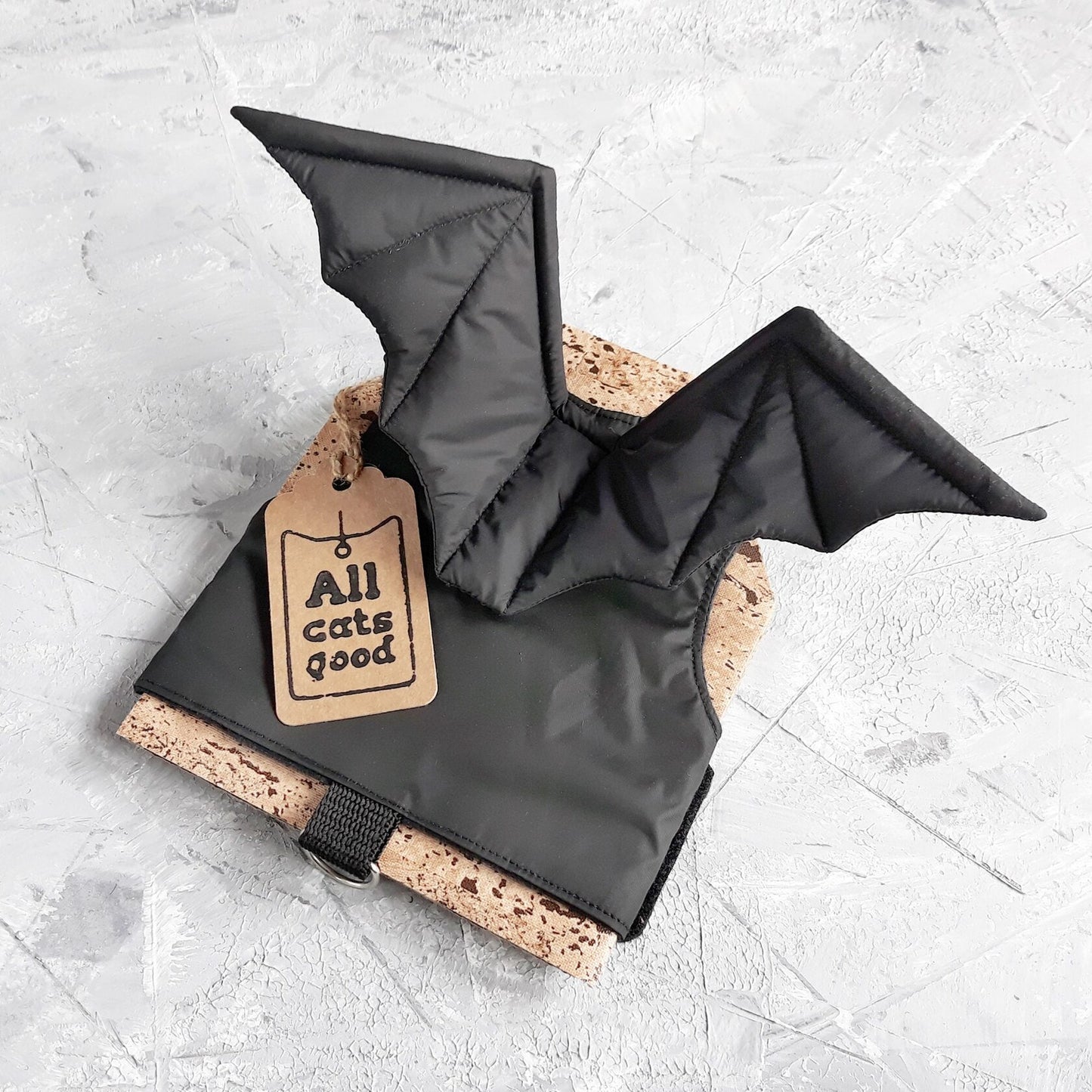 A black cat harness with bat wing accents and adjustable straps is presented with a tag that includes the phrase "Allcatsgood"