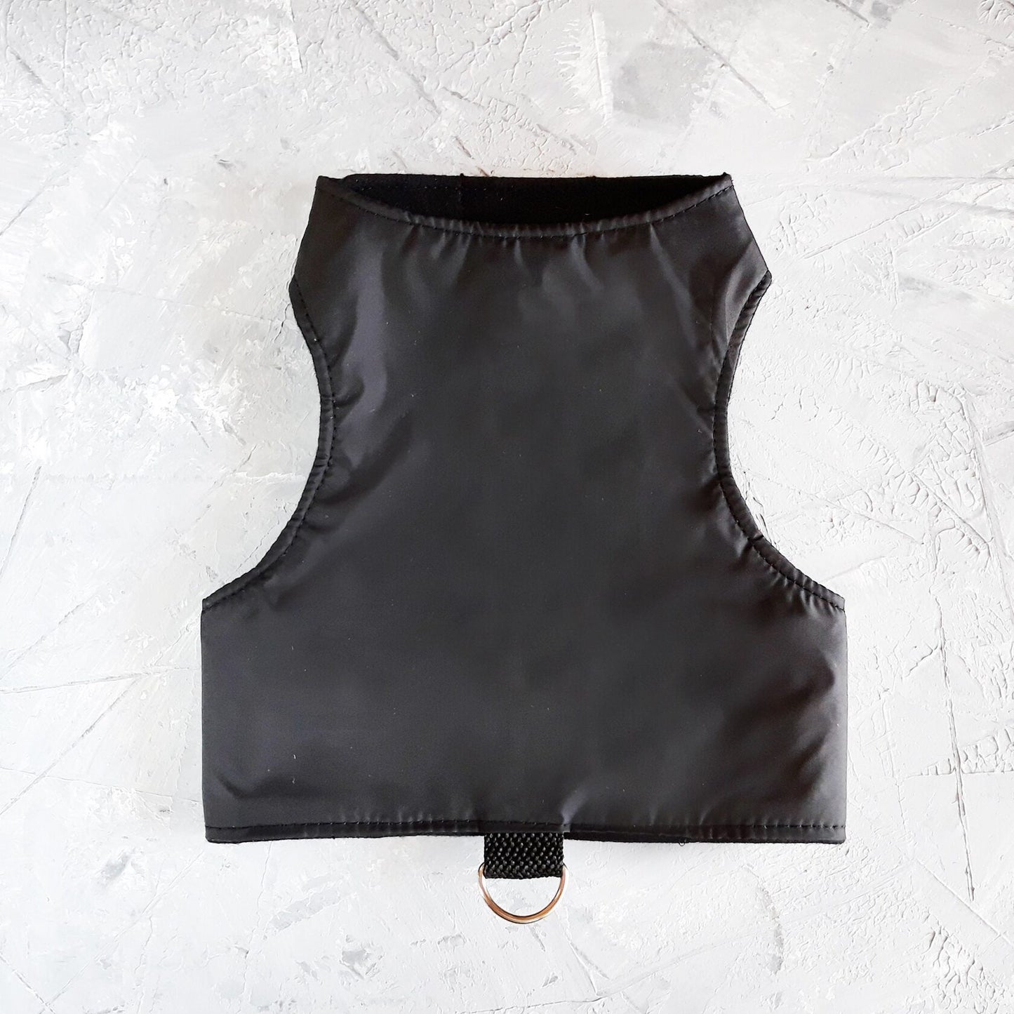 A black cat harness with a soft, fleece-lined hood and a D-ring for leash attachment.