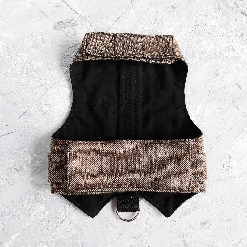 An overhead view of the inner lining of a brown tweed cat harness with a diagonal stripes pattern. The lining is a plain black fabric. A black leash attachment point with a silver D-ring is visible at the bottom.
