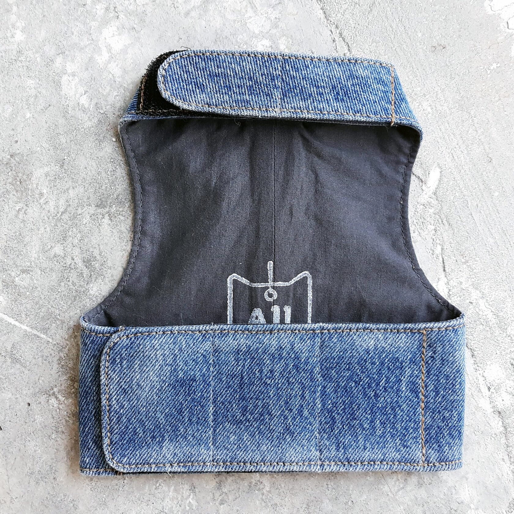 The inside of a blue denim cat harness with a dark lining and white logo.