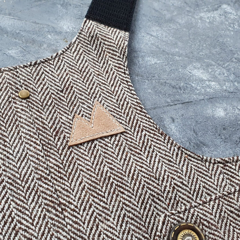 Close-up of a brown faux leather patch in the shape of three stacked triangles on a brown and cream herringbone tweed cat harness.