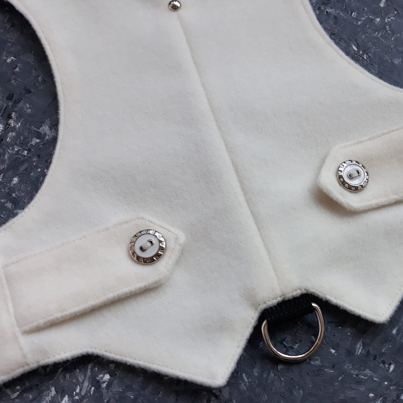 A close-up view showing the snap button fastening and the leash attachment D-ring on a white cat harness