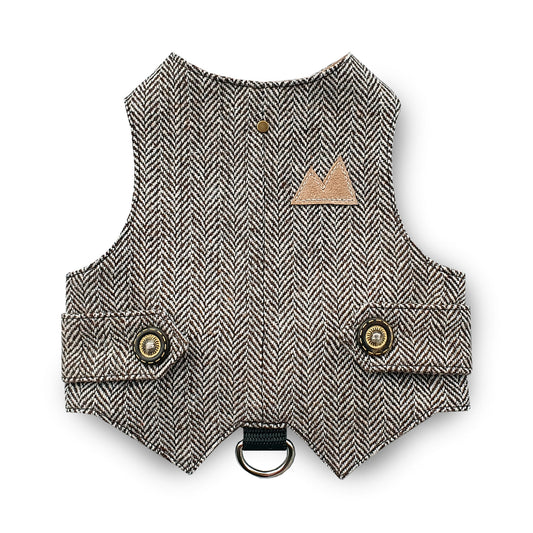 A brown and cream herringbone tweed cat harness with decorative bronze buttons, a brown faux leather mountain-shaped patch, and a black D-ring.