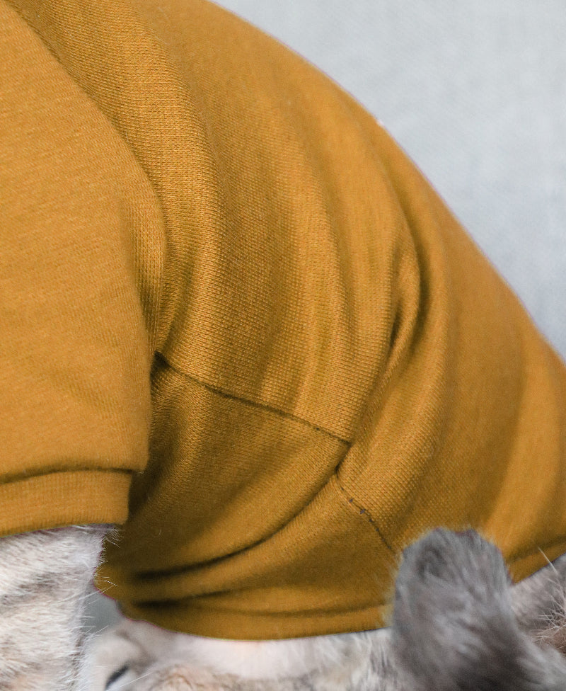 A mustard-colored sweater designed for a pet is shown on a white background