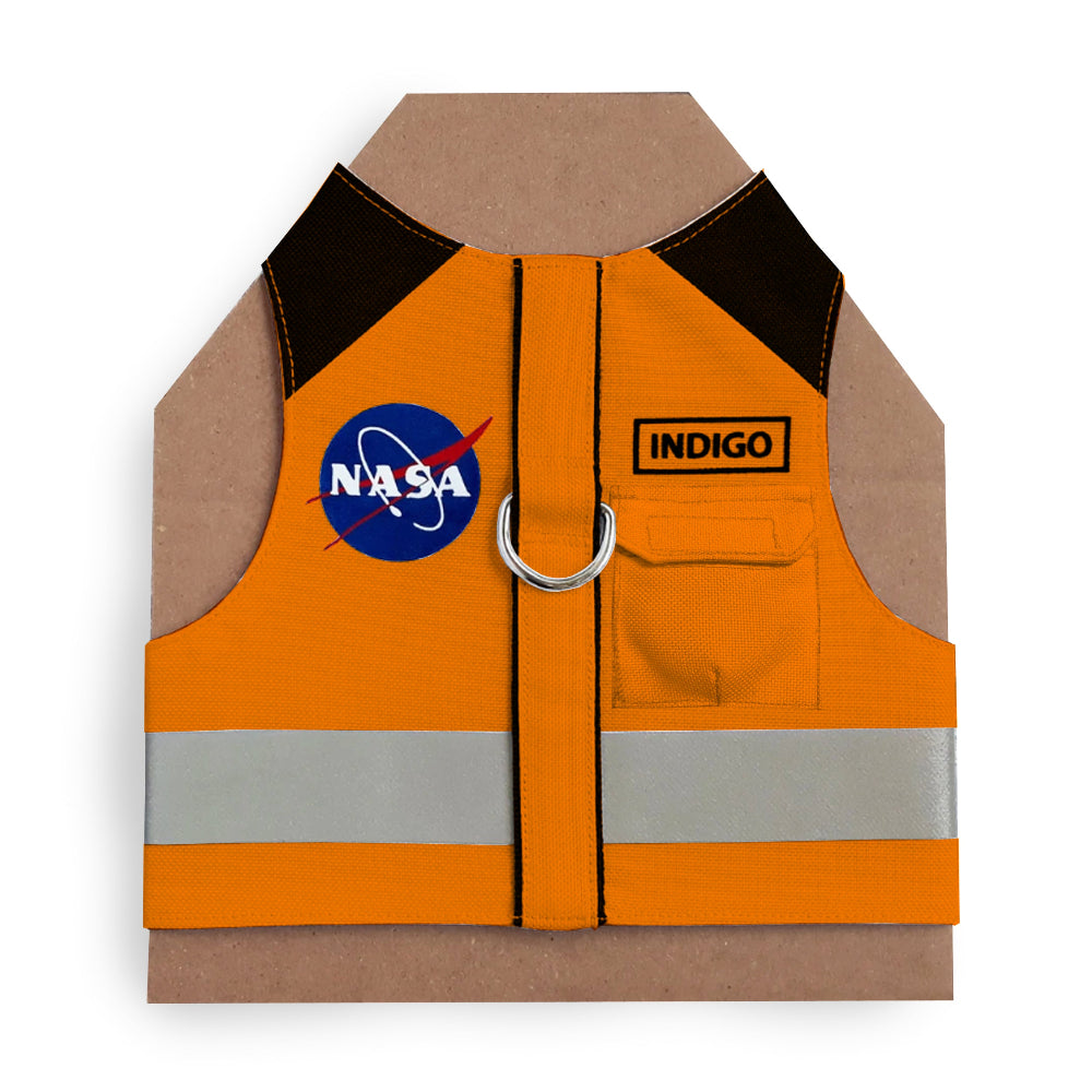 An orange cat harness with black shoulder accents, a NASA logo patch, a reflective silver stripe, and AirTag pocket
