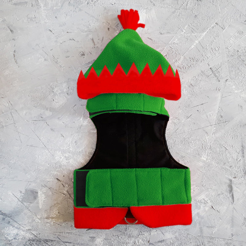 Flat lay of a green and red elf-themed cat harness with a pointed hood, red trim with jagged edges, a red tassel, and black Velcro straps.