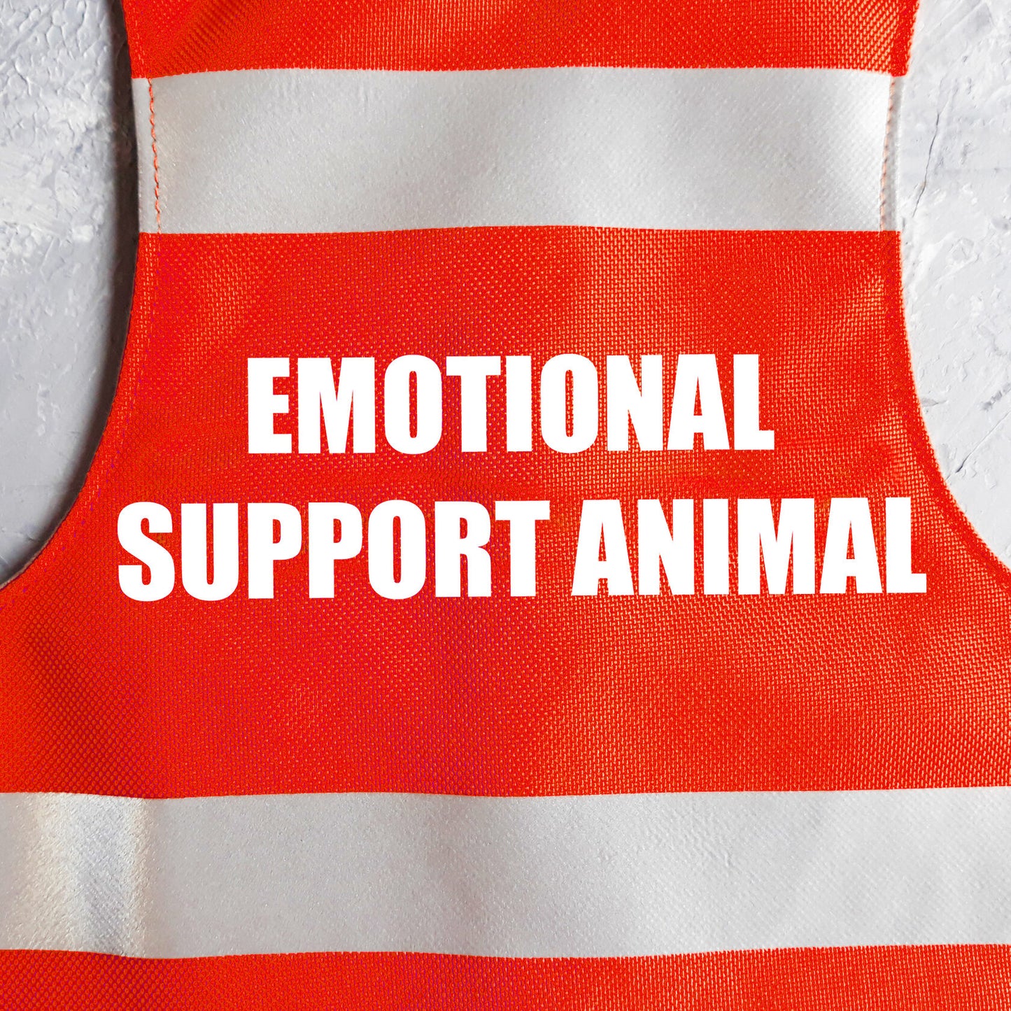 Flat lay of red safety vest for an emotional support animal, featuring two horizontal reflective silver stripes and the white text "EMOTIONAL SUPPORT ANIMAL" stacked in the center, with a black leash attachment loop and silver D-ring at the bottom.